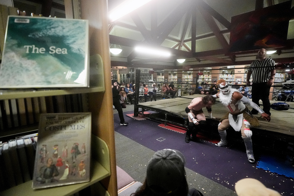 Wrestlers Jiah "the Crazy Cajun" Jewell, middle left, and El Chupacabra compete near book shelves at a Lucha Libro pro wrestling event at Benicia Public Library Saturday, May 2, 2026, in Benicia, Calif. (AP Photo/Jeff Chiu)