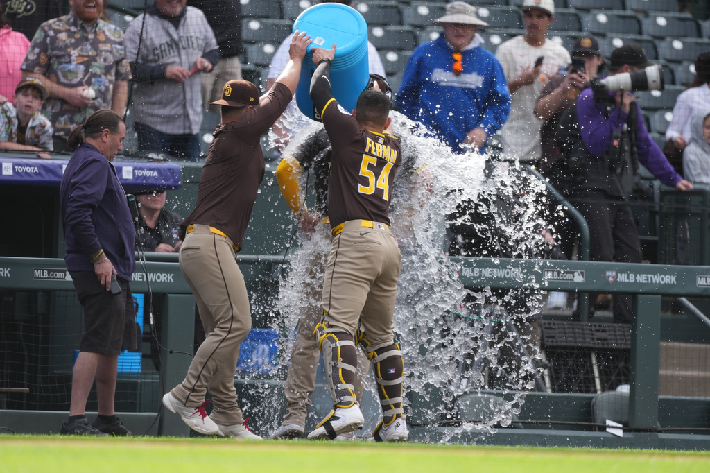 San Diego Padres first baseman Ty France, left, and catcher Freddy Fermin, right, douse Gavin Sheets as he does a television interview after leading the Padres to a victory over the Colorado Rockies in a baseball game Thursday, April 23, 2026, in Denver. (AP Photo/David Zalubowski)