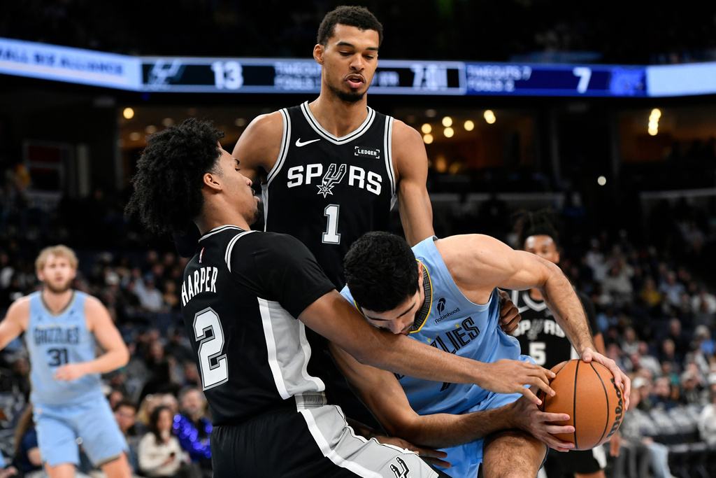 Memphis Grizzlies forward Santi Aldama, right, handles the ball against San Antonio Spurs guard Dylan Harper (2) and forward Victor Wembanyama (1) in the first half of an NBA basketball game Tuesday, Jan. 6, 2026, in Memphis, Tenn. (AP Photo/Brandon Dill)
