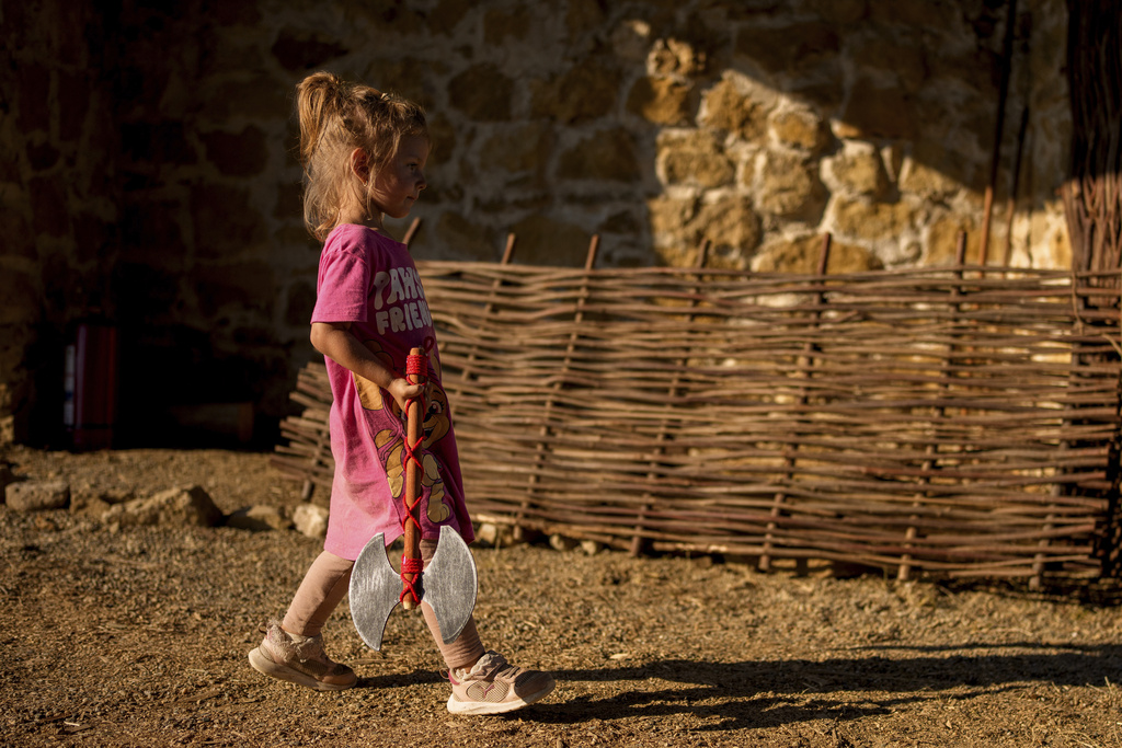 A child walks holding a replica of a battle axe in Poiana, Romania, Sunday, July 13, 2025, during the Getodava historical reenactment festival. (AP Photo/Andreea Alexandru)