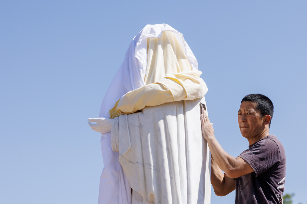 Volunteer cleans the vandalized statue of the Virgin Mary, which has been covered with a white sheet, on Apparition Hill in Medjugorje, Bosnia, Tuesday, July 28, 2026. (AP Photo)