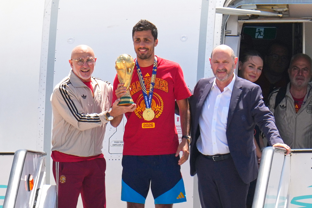 Spain's Rodrigo Hernandez holds the World Cup trophy alongside Spain head coach Luis de la Fuente, left, and Royal Spanish Football Federation President Rafael Louzan as they arrive at Madrid airport on Monday, July 20, 2026, after Spain defeated Argentina in the World Cup final. (AP Photo/Manu Fernandez)