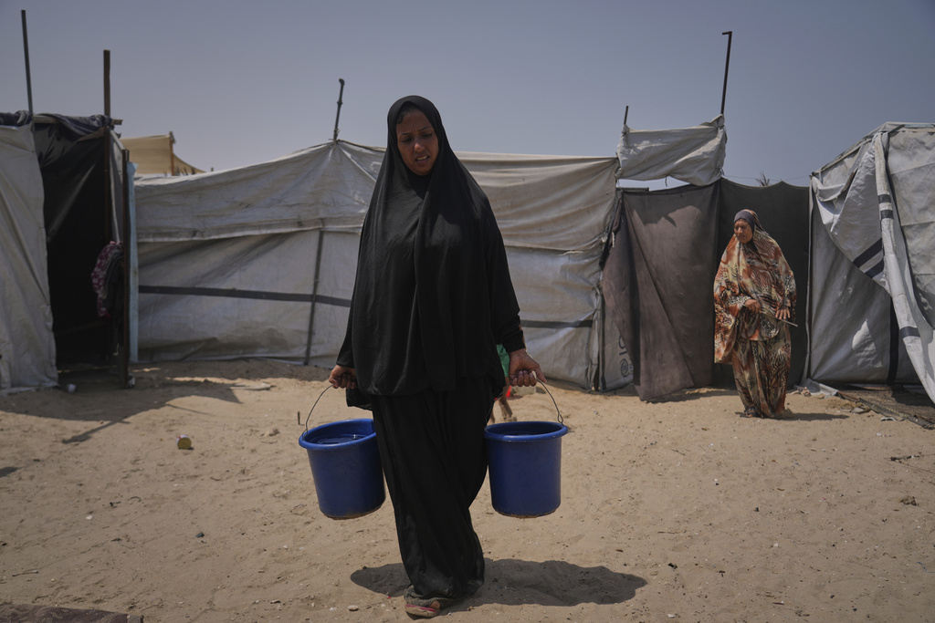 Displaced Palestinian Rana Odeh, carries buckets full of water in the next to where she takes shelter in Muwasi, Khan Younis, Gaza Strip, Wednesday, Aug, 13, 2025. (AP Photo/Abdel Kareem Hana)