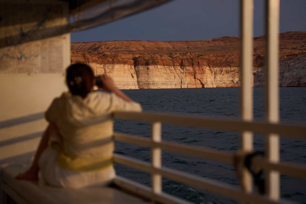 A person takes a picture during a tour on Lake Powell at the Glen Canyon National Recreation Area, Wednesday, July 15, 2026, near Page, Ariz. A bathtub ring of light minerals on the canyon wall shows the high water mark of the reservoir. (AP Photo/John Locher)