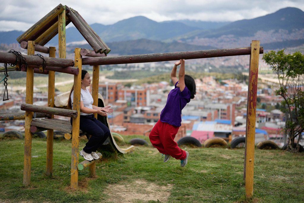 Andrea Armero, left, watches her daughter play on monkey bars in a park in Colombia, on Wednesday, Feb. 18, 2026. (AP Photo/Fernando Vergara)