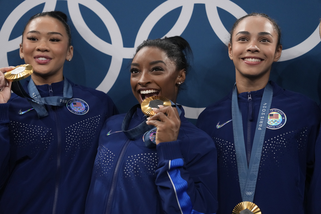 From left to right, Suni Lee, Simone Biles, Hezly Rivera celebrate after winning the gold medal during the women's artistic gymnastics team finals round at Bercy Arena at the 2024 Summer Olympics, Tuesday, July 30, 2024, in Paris, France. (AP Photo/Charlie Riedel)