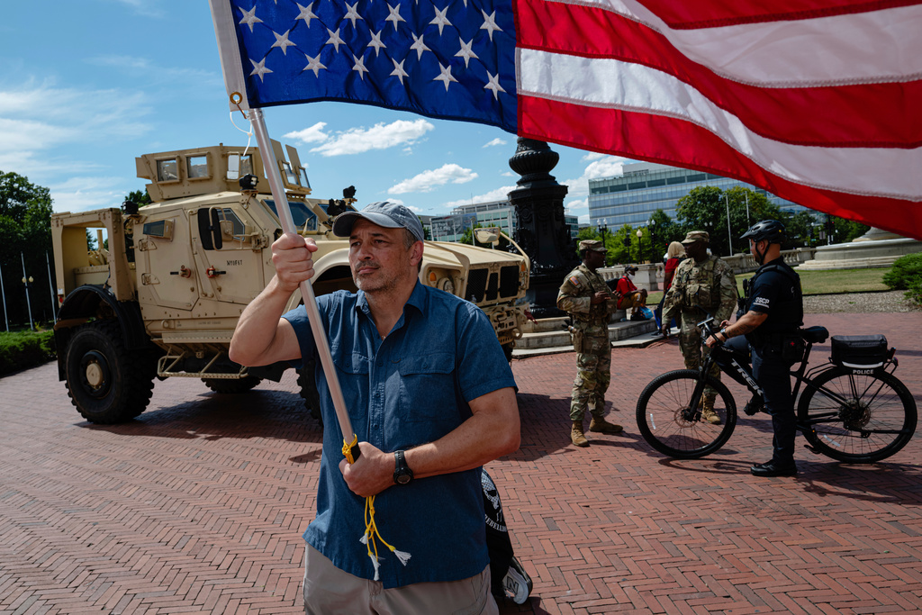 A protester holds an upside-down American flag near a DC National Guard Mine Resistant Ambush Protected vehicle (MRAP) outside of Union Station, Sunday, Aug. 31, 2025, in Washington. (AP Photo/Jon Cherry)