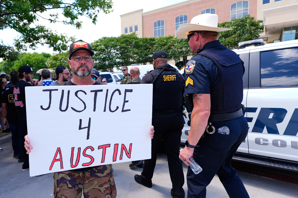 An Austin Metcalf supporter holds a sign as law enfrocement officilals walk past in front of the Collin County courthouse following the verdict in the trial was reached Tuesday, June 9, 2026, in McKinney, Texas. (AP Photo/Tony Gutierrez)
