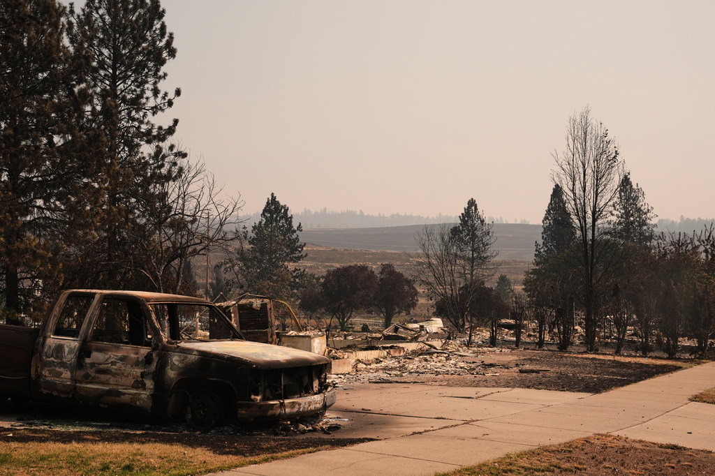 A burned truck sits in a driveway near several destroyed homes in a residential neighborhood Tuesday, Aug. 4, 2026, after a wildfire hit the northern part of Spokane, Wash. (AP Photo/Lindsey Wasson)