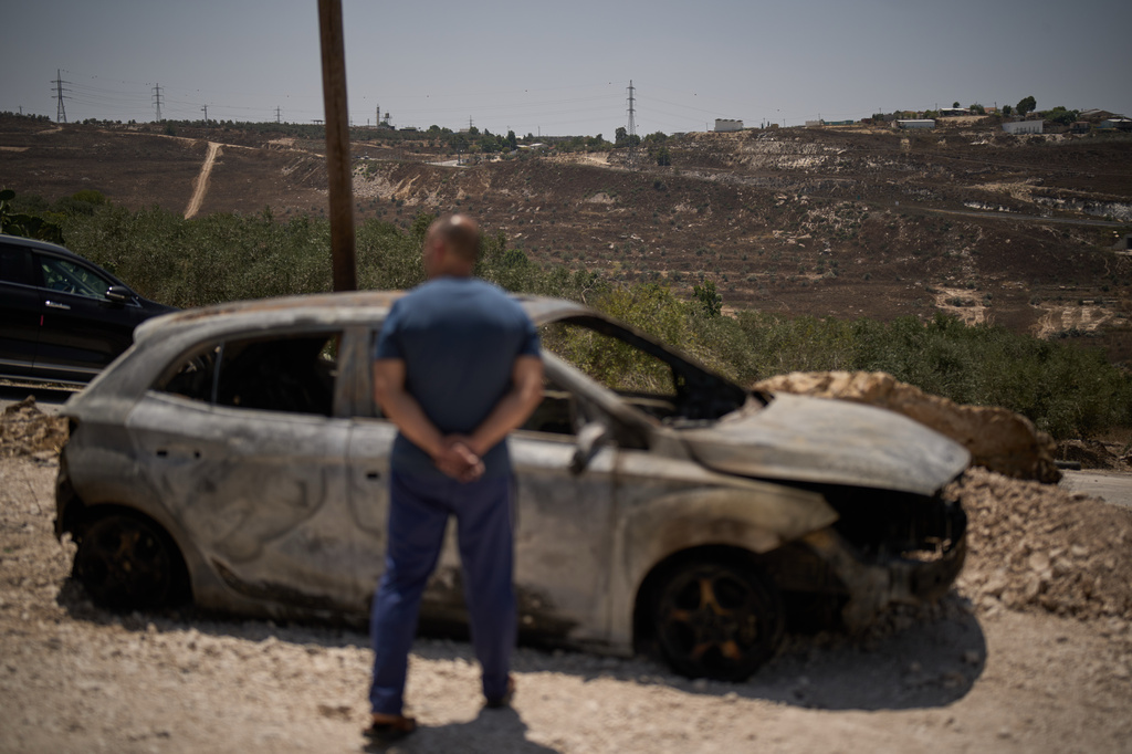 With the Israeli settlement of Khavat Gilad in the background, a Palestinian man stands in front of a burned car following an attack by Israeli settlers the previous day in the village of Sarra, near the West Bank city of Nablus, Saturday, July 25, 2026. (AP Photo/Leo Correa)