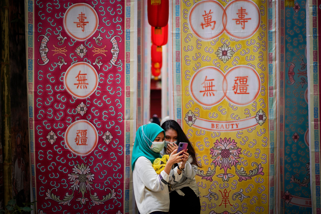 FILE - Two Malay girls check a mobile phone at a fabric installation decoration at Kwai Chai Hong, the Chinatown area in downtown Kuala Lumpur, Malaysia, Tuesday, March 30, 2021. (AP Photo/Vincent Thian, File)