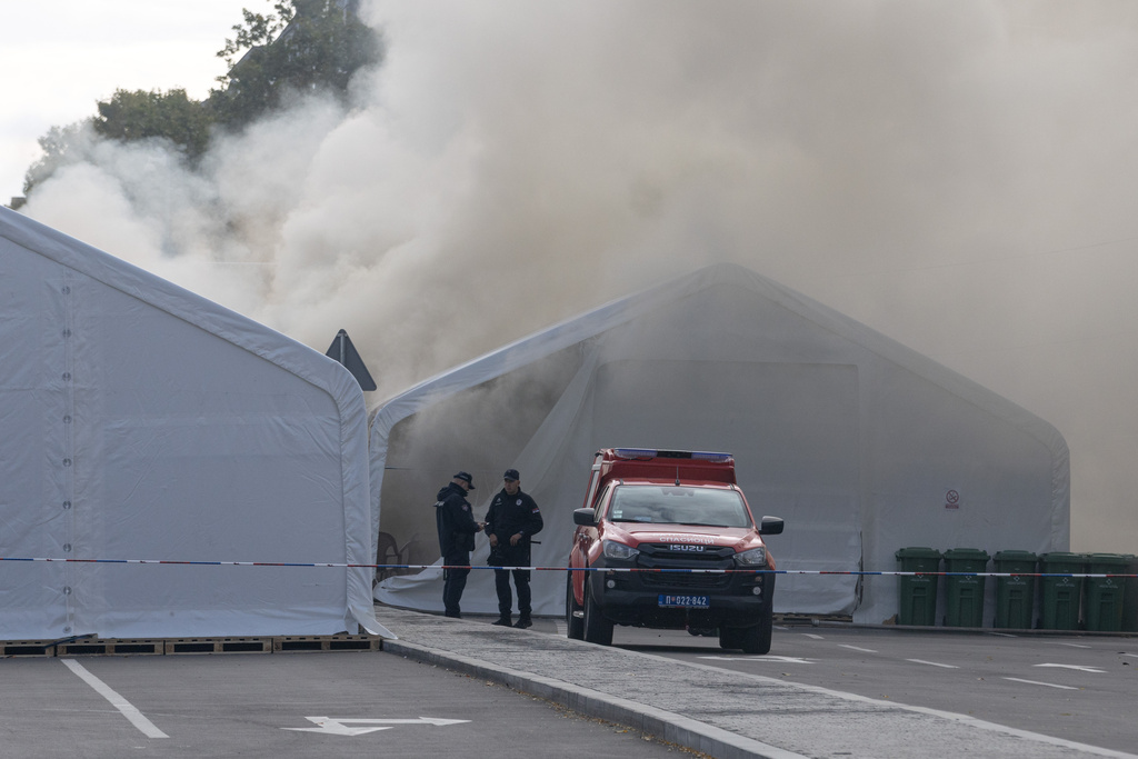 Police officers stand on a street as a fire is localized in the government supporters' camp outside the Serbian parliament in Belgrade, Serbia, Wednesday, Oct. 22, 2025. (AP Photo/Marko Drobnjakovic)