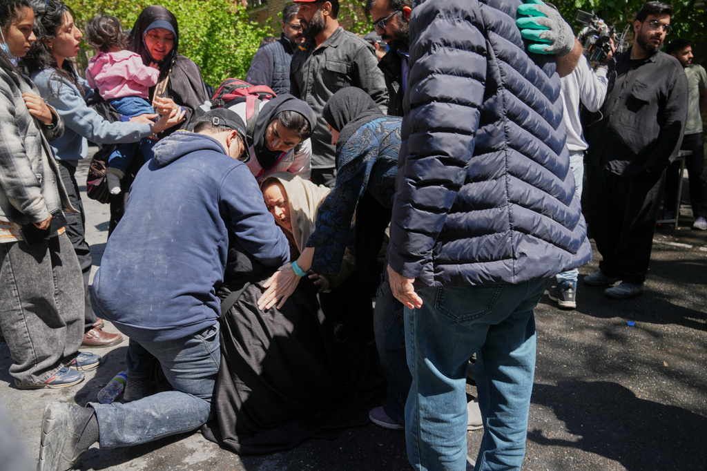 Bystanders try to comfort and assist a woman as she reacts near the site of a strike that, according to a security official at the scene, destroyed half of the Khorasaniha Synagogue and nearby residential buildings in Tehran, Iran, Tuesday, April 7, 2026. (AP Photo/Francisco Seco)