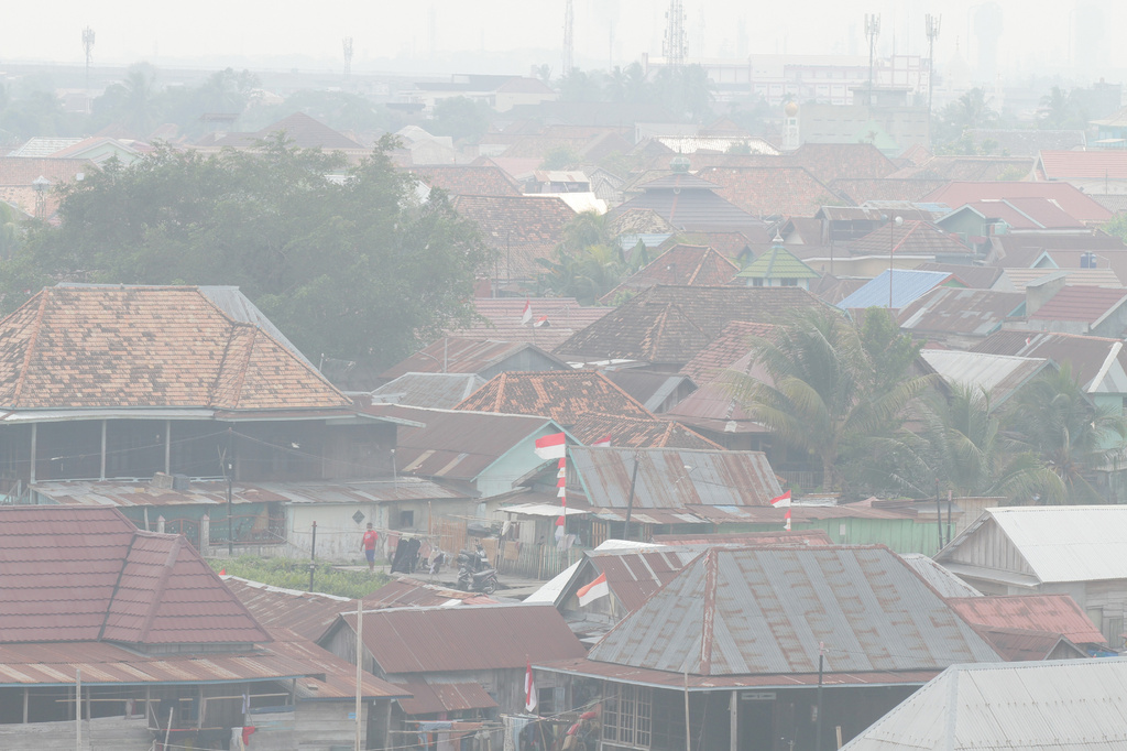A man stands among houses as haze from wildfires blankets the city of Palembang, South Sumatra, Indonesia, Tuesday, Aug. 25, 2026. (AP Photo/Muhammad Hatta)