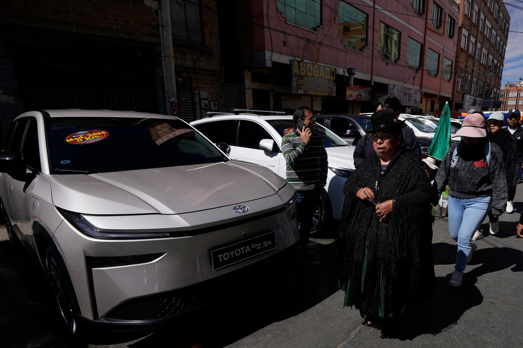 People walks past electric cars displayed for sale at "La Feria de la 16 de Julio," in El Alto, Bolivia, Sunday, April 19, 2026. (AP Photo/Juan Karita)