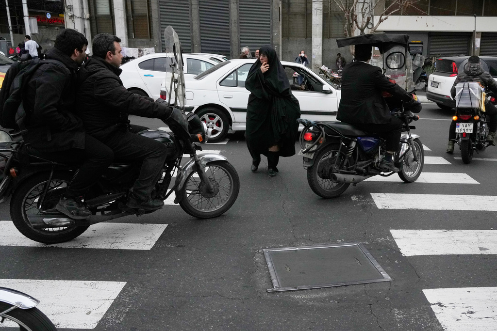 A woman crosses a square as motorbikes ride past in downtown Tehran, Iran, Tuesday, Feb. 24, 2026. (AP Photo/Vahid Salemi)