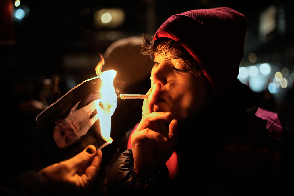 CORRECTS MONTH - A protester lights a cigarette off a burning poster of Iran's Supreme Leader Ayatollah Ali Khamenei during a demonstration in Berlin, Germany, in support of the nationwide mass protests in Iran against the government, Wednesday, Jan. 14, 2026. (AP Photo/Ebrahim Noroozi)