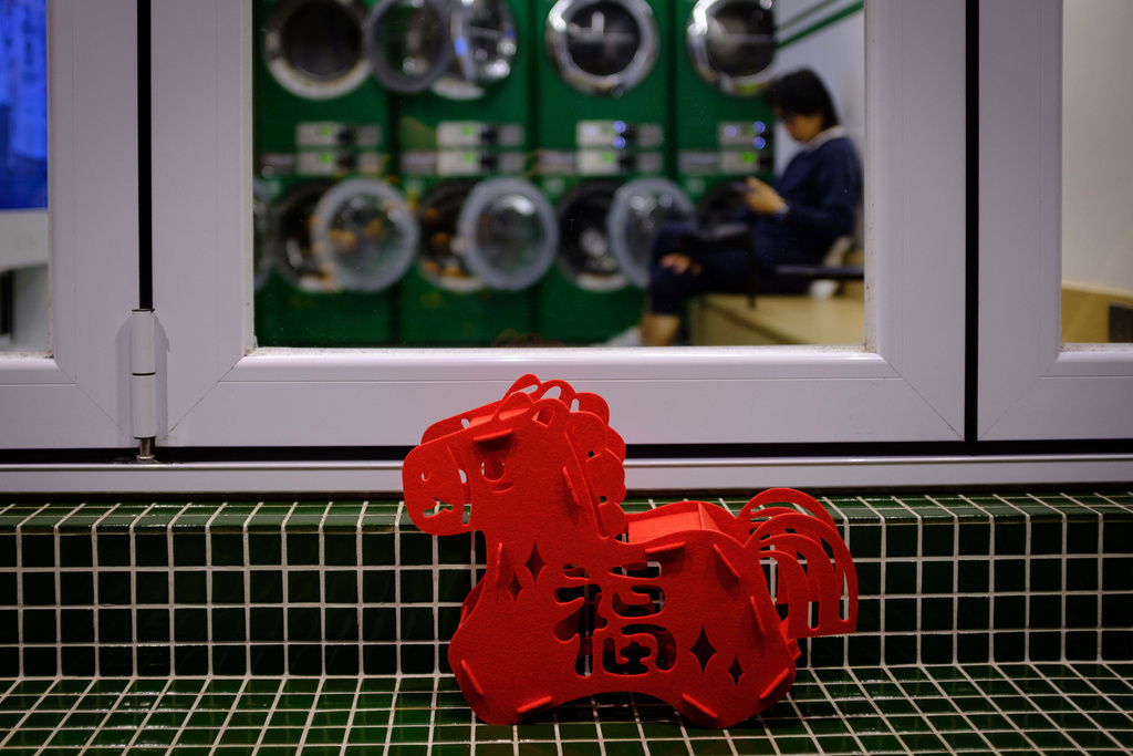 A person waits inside a laundromat as a red Lunar New Year decoration sits on a tiled bench on the first day of the Lunar New Year in Hong Kong, Feb. 17, 2026. (AP Photo/May James)