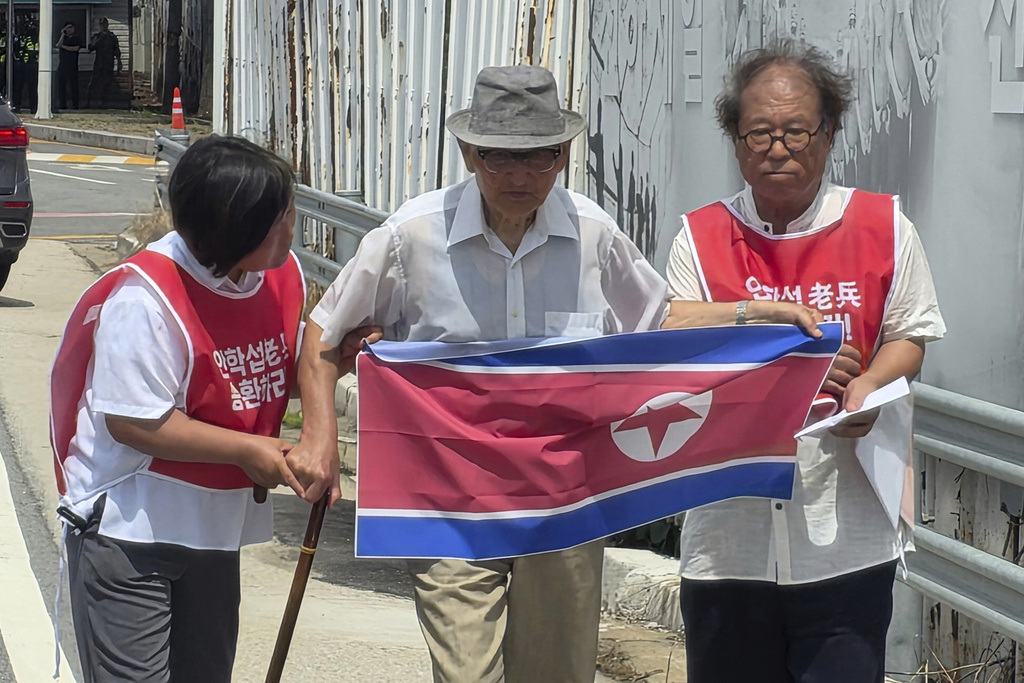 Ahn Hak-sop, center, a 95-year-old former North Korean soldier who spent decades imprisoned in the South, holds a North Korean flag near the Unification Bridge which leads to the Panmunjom in the Demilitarized Zone in Paju, South Korea, Wednesday, Aug. 20, 2025. (Shim Min-kyu/Yonhap via AP)