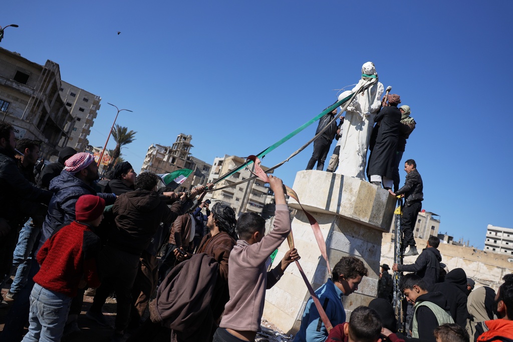 Local supporters of the Syrian government deface and attempt to topple a sculpture depicting a Kurdish woman a day after Syrian government troops took control of the area from the Syrian Democratic Forces (SDF), in Raqqa, northeastern Syria, Monday, Jan. 19, 2026. (AP Photo/Omar Albam)