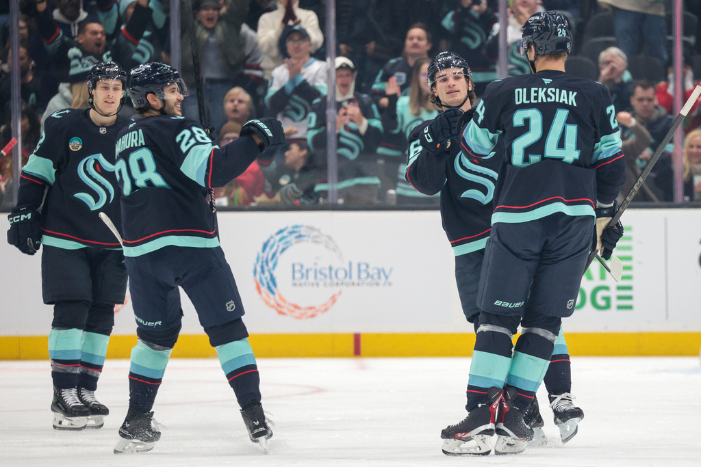 Seattle Kraken defenseman Jamie Oleksiak (24) celebrates with center Ryan Winterton, second right, defenseman Joshua Mahura and left wing Tye Kartye, left, after scoring during the second period of an NHL hockey game against the Chicago Blackhawks Monday, Nov. 3, 2025, in Seattle. (AP Photo/Jason Redmond)
