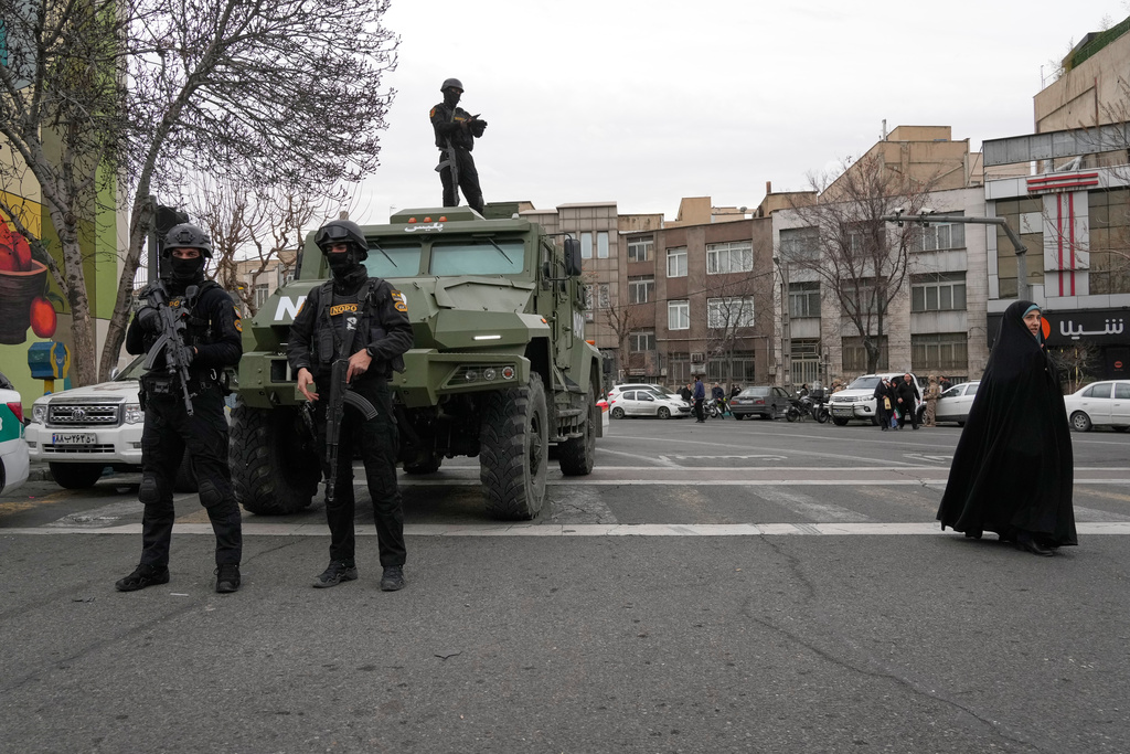 Policemen stand guard during an annual rally marking 1979 Islamic Revolution as a woman walks at right at the Azadi (Freedom) St. Tehran, Iran, Wednesday, Feb. 11, 2026. (AP Photo/Vahid Salemi)