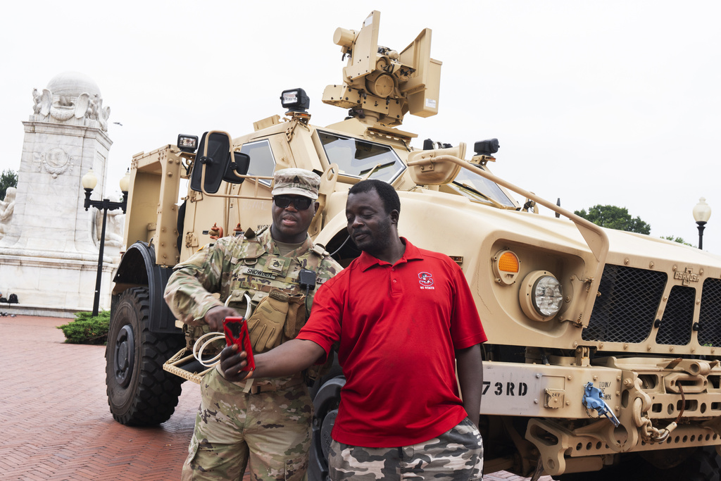 District of Columbia Army National Guard Staff Sgt. Snowden, left, shows James Maseno of Grandal, Md., how to take a selfie next to an M-ATV infantry mobility vehicle, outside the Union Station in Washington, Monday, Aug. 18, 2025. (AP Photo/Manuel Balce Ceneta)