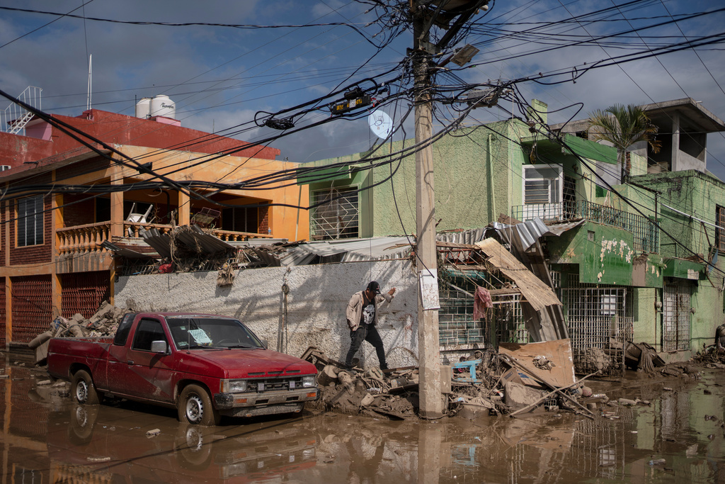 A local walks along a mud-covered street in Poza Rica, Veracruz state, Mexico, on Tuesday, Oct. 14, 2025, after landslides and torrential rain. (AP Photo/Felix Marquez)