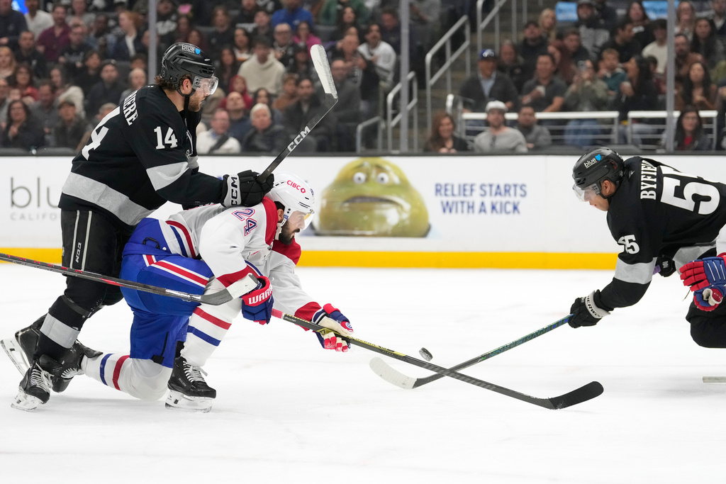 Montréal Canadiens center Phillip Danault, center, tries to shoot the puck while under pressure from Los Angeles Kings right wing Alex Laferriere, left, and right wing Quinton Byfield during the second period of an NHL hockey game Saturday, March 7, 2026, in Los Angeles. (AP Photo/Mark J. Terrill)