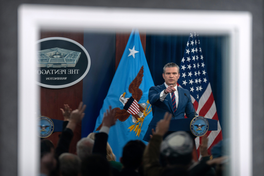 Defense Secretary Pete Hegseth, reflected in a window, gestures during a press briefing at the Pentagon, Monday, March 2, 2026, in Washington. (AP Photo/Mark Schiefelbein)