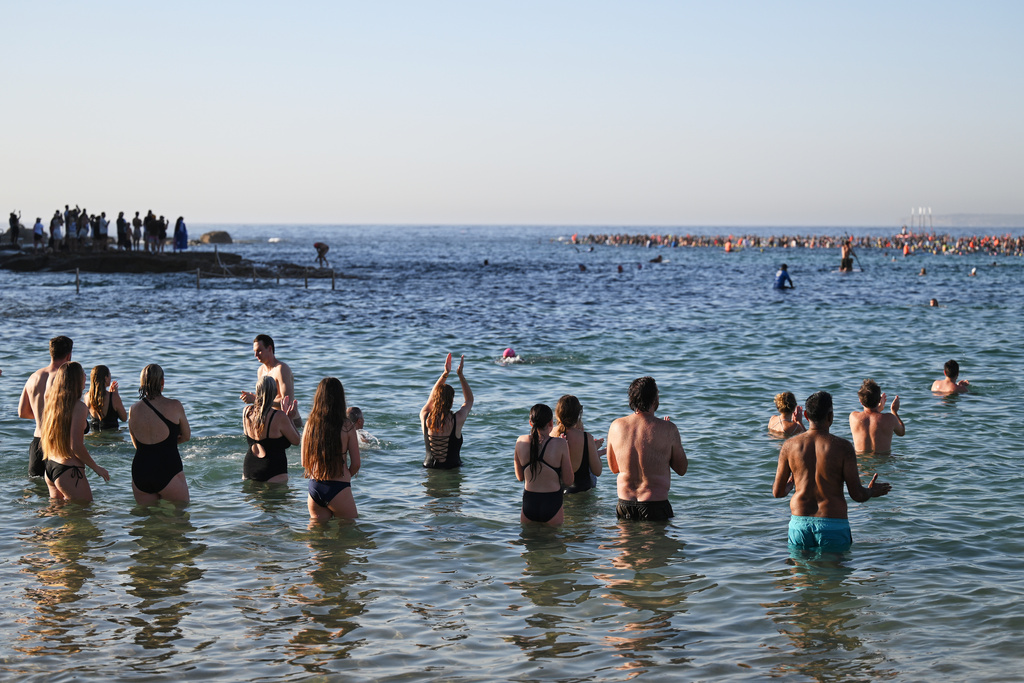 Surfers and swimmers head out to the ocean as a tribute following Sunday's shooting at Bondi Beach, in Sydney, Friday, Dec. 19, 2025. (AP Photo/Steve Markham)