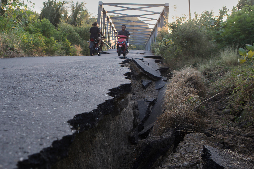 Motorists ride their motorbikes near an earthquake-damaged road in North Lamba Leda, East Nusa Tenggara province, Indonesia, Tuesday, Aug. 18, 2026. (AP Photo/Firdia Lisnawati)