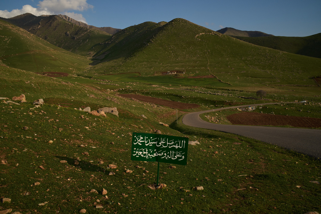 A sign displays a prayer that reads in Arabic: "Oh Allah, send blessings upon our prophet, and upon his family, and companions", on a road near the village of Gulp, Iraq, Tuesday, March 17, 2026. (AP Photo/Leo Correa)