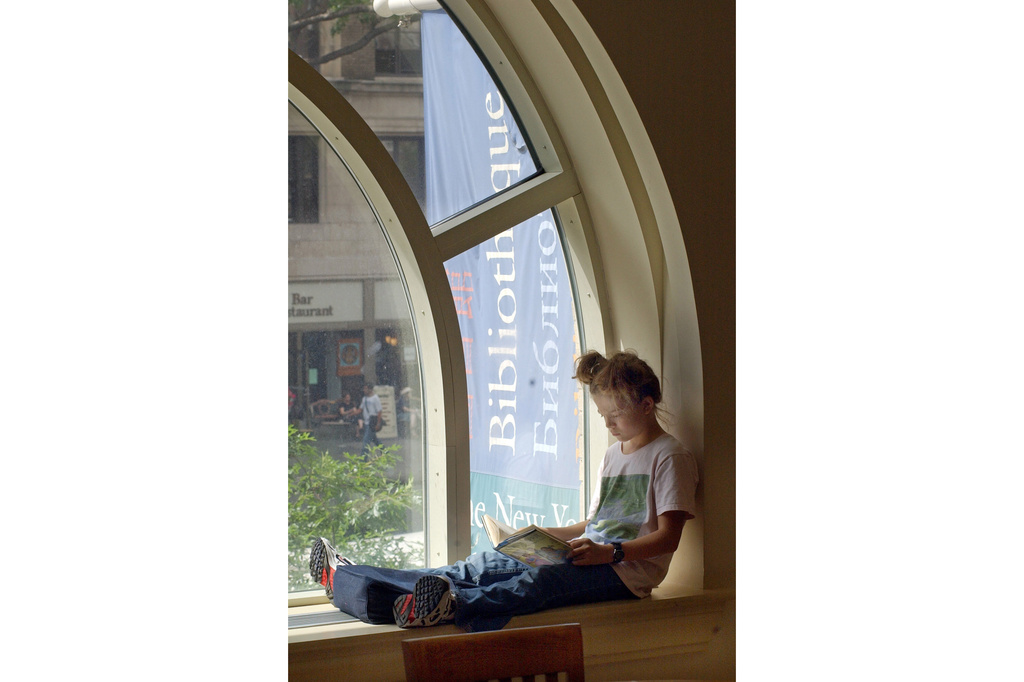 FILE - A young girl reads a book while sitting in a window of the Morningside Heights branch of the New York Public Library on July 29, 2003. (AP Photo/Richard Drew, file)