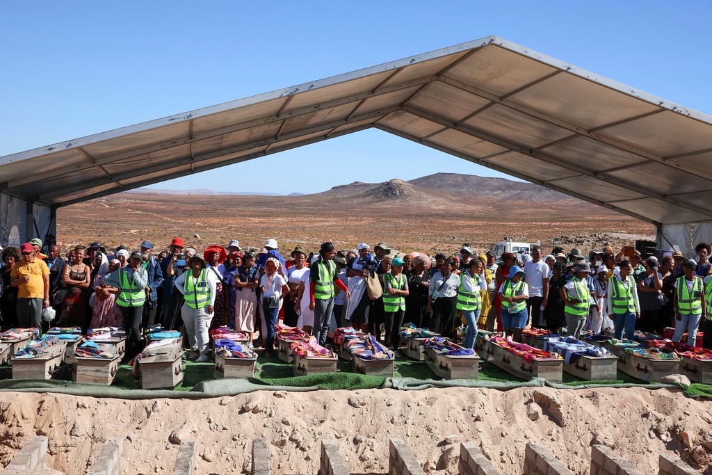In this photo provided by the South African Government Communications and Information Services, families and community members stand behind the coffins during a reburial of remains of dozens of Africans whose bodies were dug up and sent to Europe for scientific research long ago, in Steinkopf, South Africa, Monday, March 23, 2026. (Jairus Mmutle/GCIS via AP)