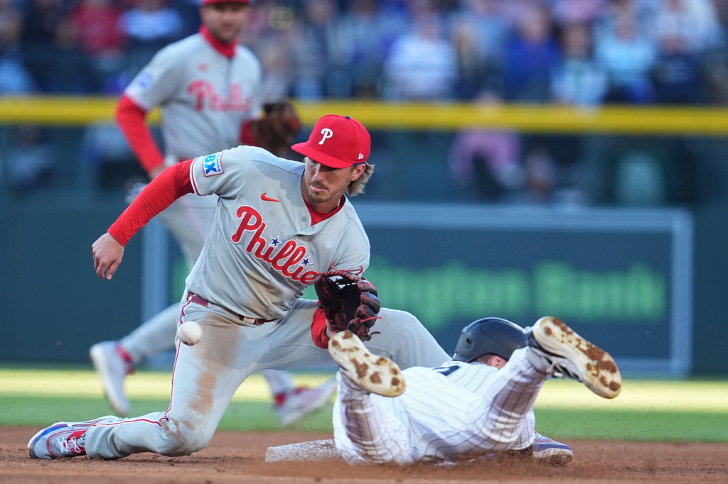 Philadelphia Phillies second baseman Bryson Stott, left, fields a throw to tag out Colorado Rockies' Brenton Doyle, right, who tries to steal second in the first inning of a baseball game Saturday, April 4, 2026, in Denver. (AP Photo/David Zalubowski)