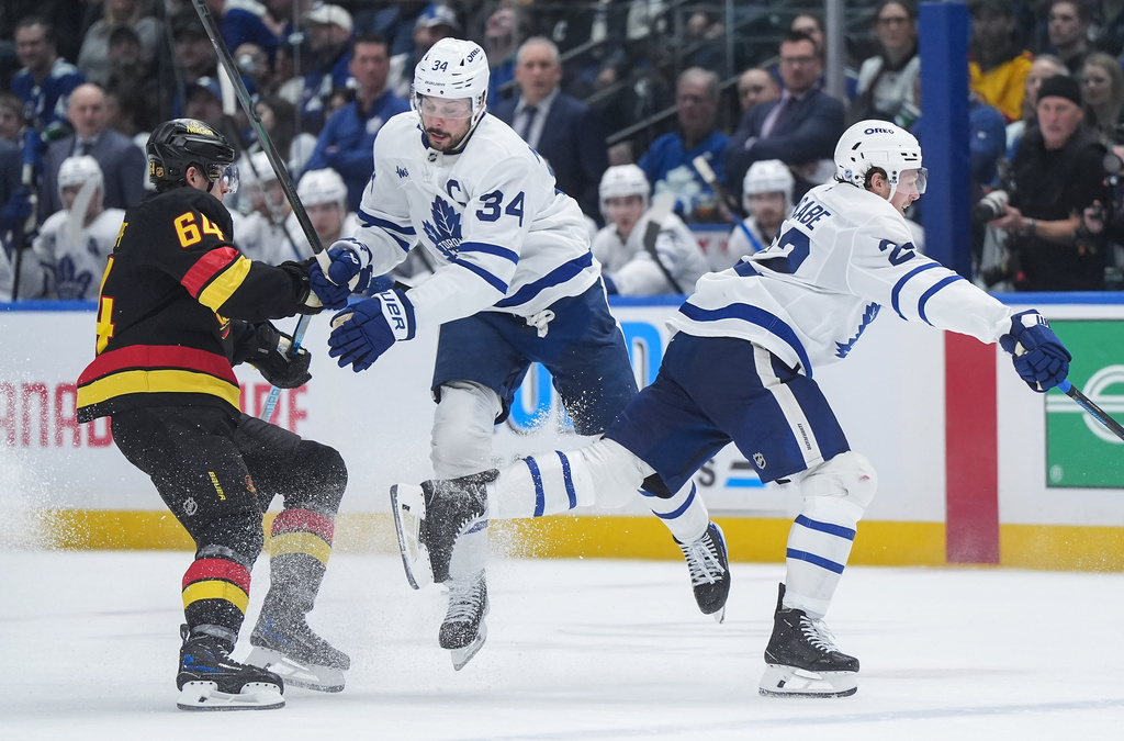Toronto Maple Leafs' Jake McCabe (22) and Auston Matthews (34) collide in front of Vancouver Canucks' David Kampf (64) during the second period of an NHL hockey game in Vancouver, British Columbia, Saturday, Jan. 31, 2026. (Darryl Dyck/The Canadian Press via AP)