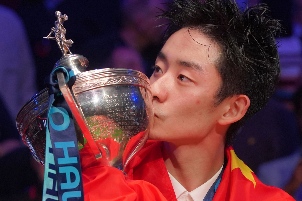 China's Wu Yize poses for the media with the trophy, wearing the national flag of China, after winning the World Snooker Championship defeating England's Shaun Murphy in Sheffield, England, Monday, May 4, 2026.(AP Photo/Ian Hodgson)