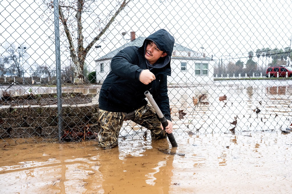 Dekoda Cruz works to clear a drain following heavy rains on Monday, Dec. 22, 2025, in Redding, Calif. (AP Photo/Noah Berger)