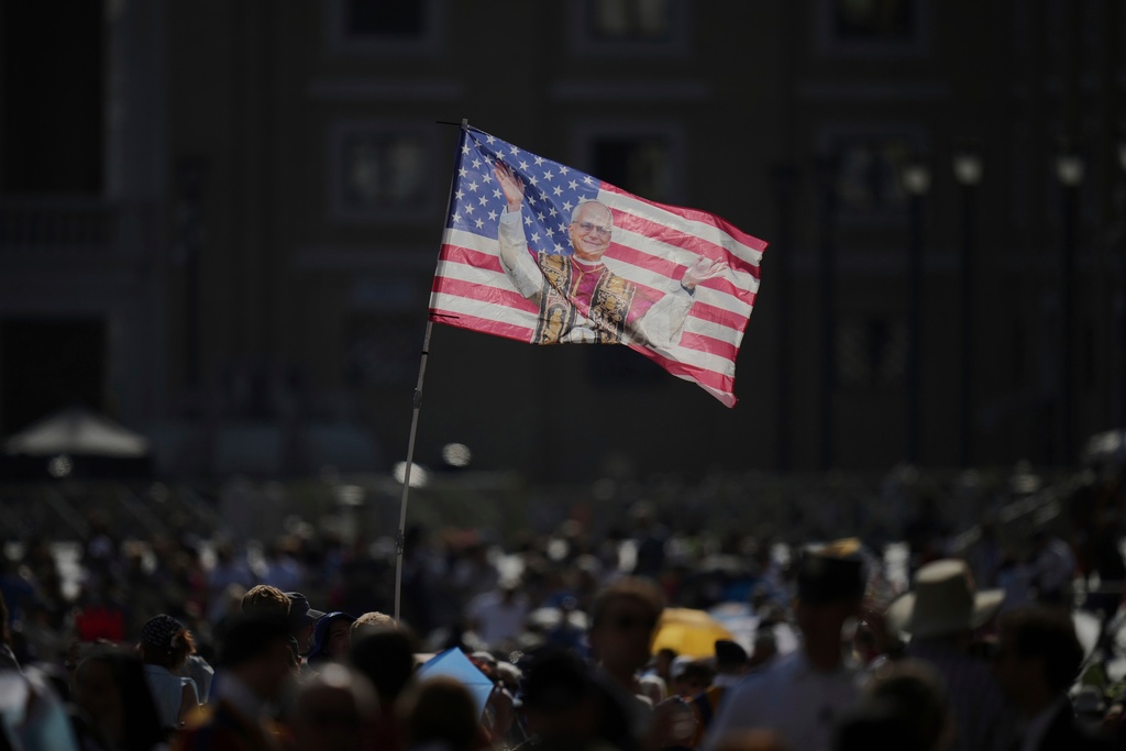FILE - People wave a flag prior to the arrival of Pope Leo XIV for his weekly general audience in St. Peter's Square at the Vatican, June 18, 2025. (AP Photo/Alessandra Tarantino, File)