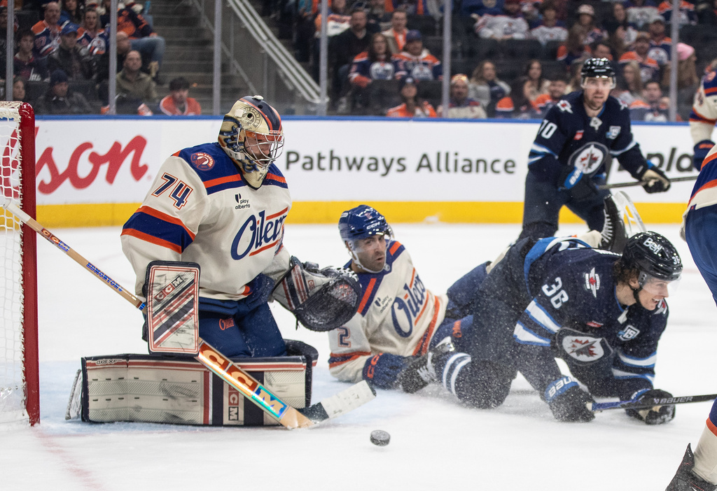Winnipeg Jets' Morgan Barron (36) and Edmonton Oilers' Evan Bouchard (2) battle in front as goalie Stuart Skinner (74) makes the save during third period NHL action, in Edmonton on Saturday, Dec. 6, 2025. (Jason Franson/The Canadian Press via AP)