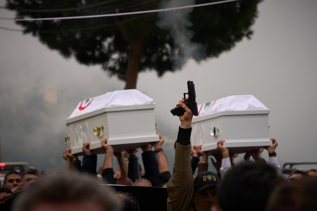 A gunman fires his gun as men carry the coffins with the bodies of Pierre Mouawad, an official with the anti-Hezbollah Lebanese Forces party, and his wife during their funeral in Yahshush, in Lebanon, Tuesday, April 7, 2026. (AP Photo/Emilio Morenatti)