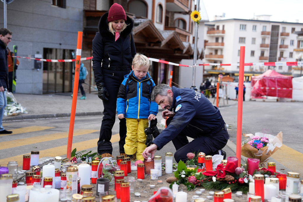 A police officer helps a boy to light a candle near the sealed off Le Constellation bar in Crans-Montana, Swiss Alps, Switzerland, Friday, Jan. 2, 2026, where a devastating fire left dead and injured during the New Year's celebrations. (AP Photo/Baz Ratner)