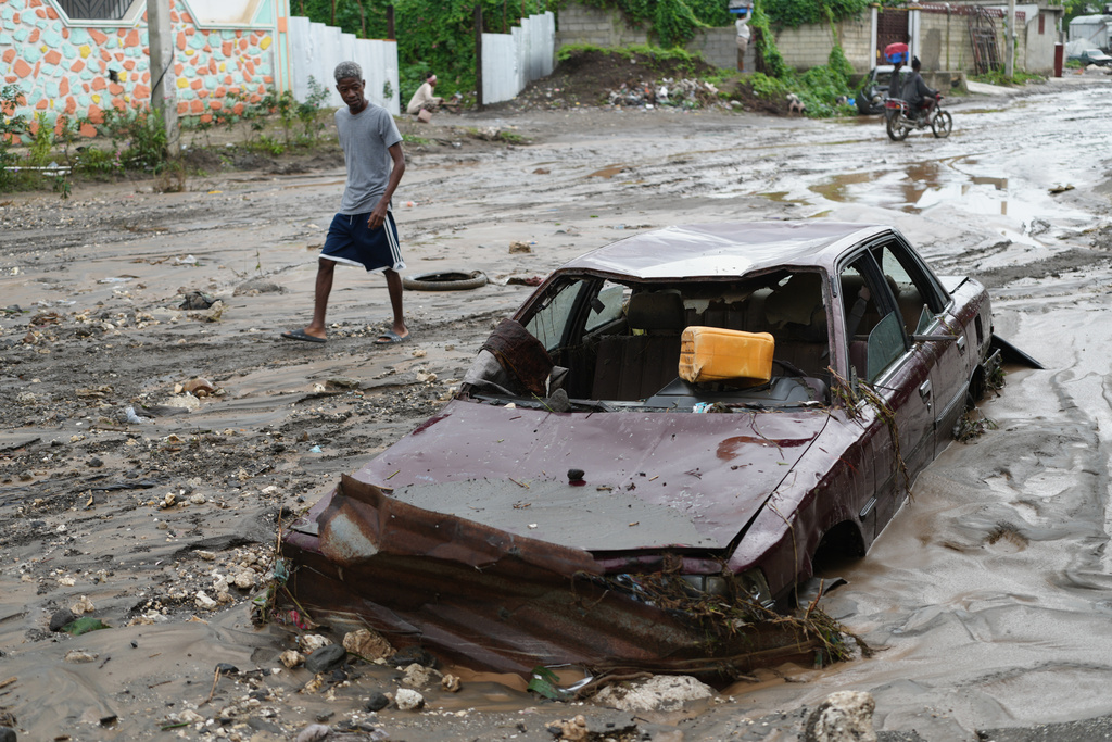 A pedestrian looks a at flooded car in the aftermath of Hurricane Melissa in Petit-Goave, Haiti, Thursday, Oct. 30, 2025. (AP Photo/Odelyn Joseph),