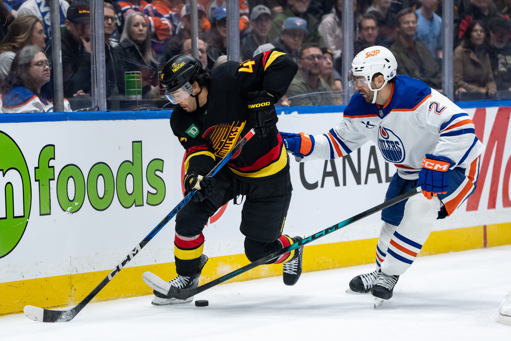 Vancouver Canucks' Kiefer Sherwood (44) and Edmonton Oilers' Evan Bouchard (2) vie for the puck during third period NHL hockey action in Vancouver, British Columbia, Sunday, Oct. 26, 2025. (Ethan Cairns/The Canadian Press via AP)