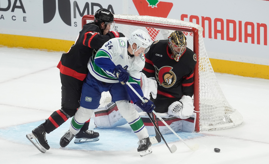 Vancouver Canucks center, Aatu Raty (54) tries to tip the puck past Ottawa Senators goaltender Leevi Merilainen (1) as he is pressured by defenseman Jordan Spence (10) during first period NHL action in Ottawa, Tuesday, Jan. 13, 2026. (Adrian Wyld/The Canadian Press via AP)