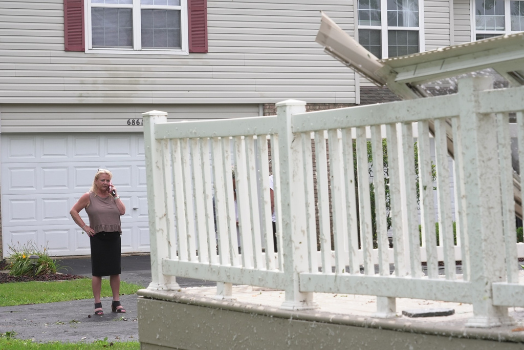 Kerry Hourigan speaks on the phone after reviewing damage a storm caused to her home in Tinley Park, Ill., Tuesday, Aug. 11, 2026. (AP Photo/Laura Bargfeld)