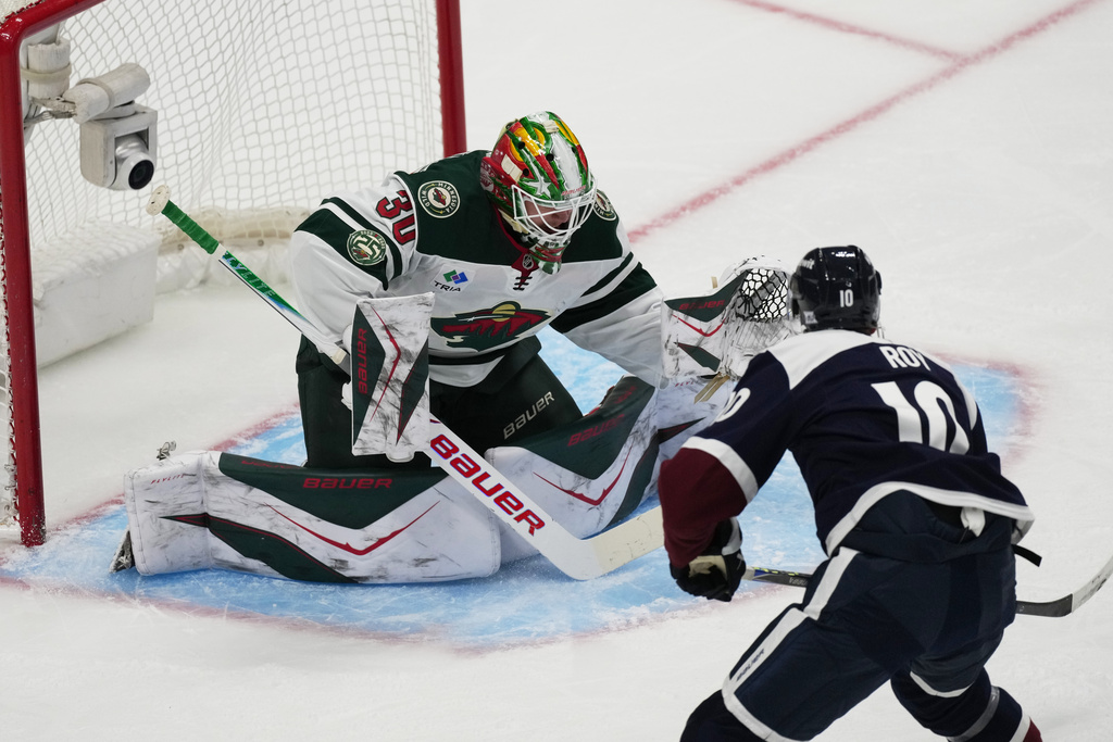 Colorado Avalanche center Nicolas Roy, front, puts a shot on Minnesota Wild goaltender Jesper Wallstedt in the first period of an NHL hockey game, Sunday, March 8, 2026, in Denver. (AP Photo/David Zalubowski)