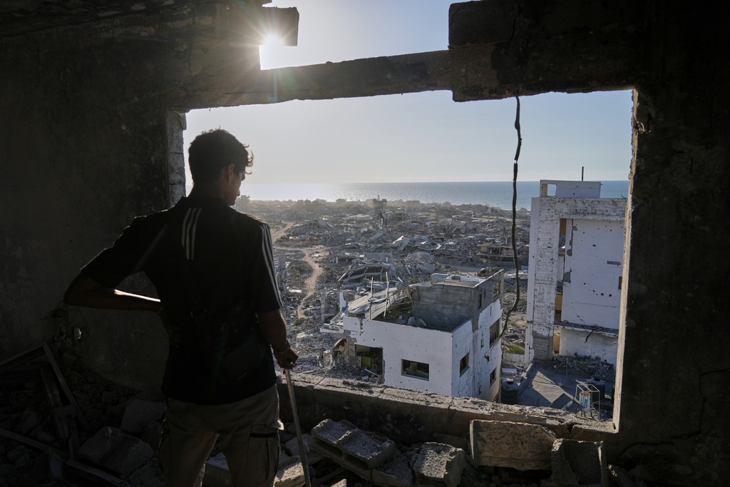 A man looks out from his damaged apartment at the destruction in his neighborhood in Gaza City, Friday, Oct. 10, 2025, after returning home following an agreement between Israel and Hamas on a ceasefire and the release of remaining hostages. (AP Photo/Jehad Alshrafi)