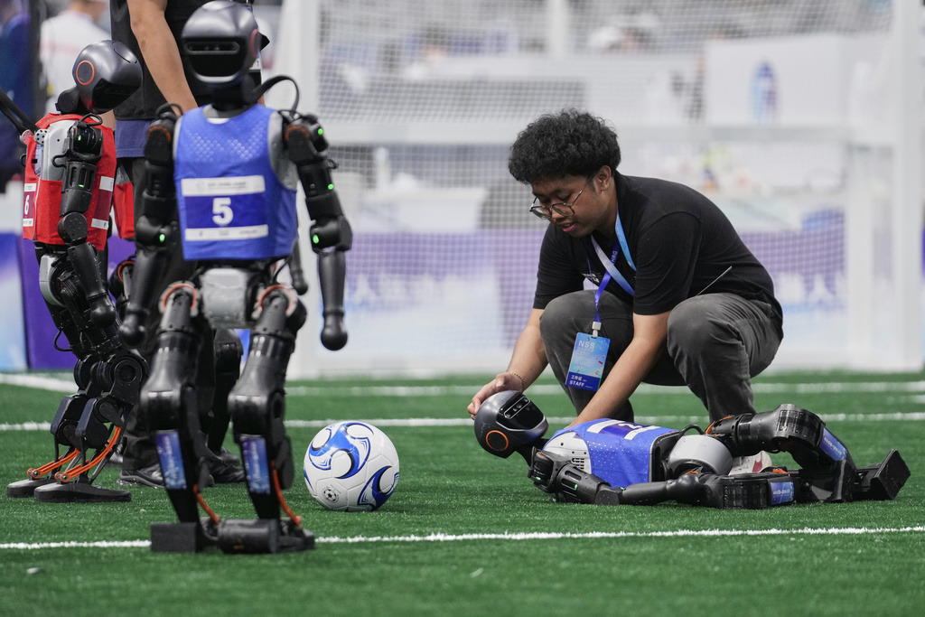 A technician assists a robot that fell during a soccer match at the World Humanoid Robot Games in Beijing, China, Friday, Aug. 15, 2025. (AP Photo/Mahesh Kumar A.)